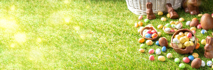 Easter egg hunting background. Various candy and chocolate Easter eggs, bunny and rabbits with basket for eggs on green grass park or garden background