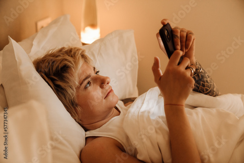 Canvastavla Young woman using smartphone while laying on bed at home