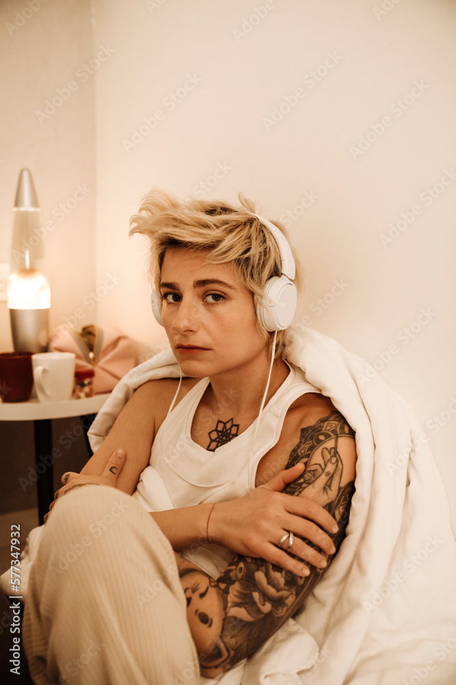 Young blonde woman listening music with headphones while sitting at home
