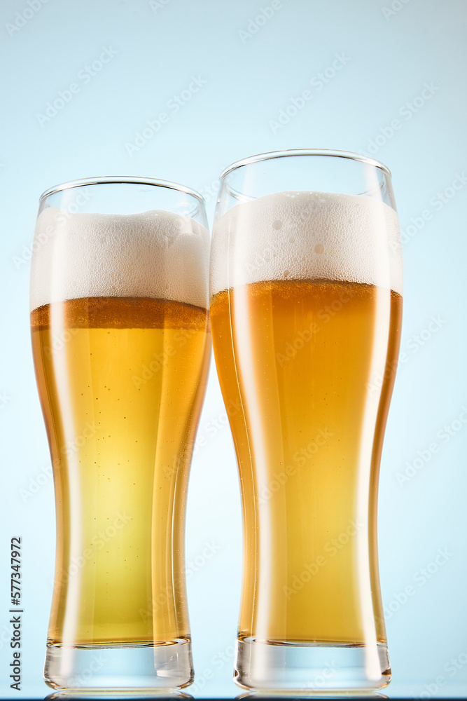 Fizzy yellow beer poured to tall glasses on light blue. Fizzy yellow beer poured to tall glasses on light blue.