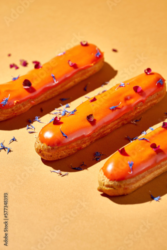 Three eclairs with orange glaze and custard on an orange background. Creative layout. Creative food poster