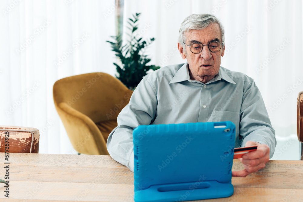 old man sitting at pad making payments on line with credit card and tablet old man sitting at pad making payments on line with credit card and tablet