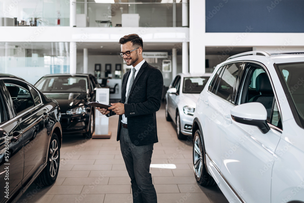 Good looking, cheerful and friendly salesman poses in a car salon or showroom. Good looking, cheerful and friendly salesman poses in a car salon or showroom.