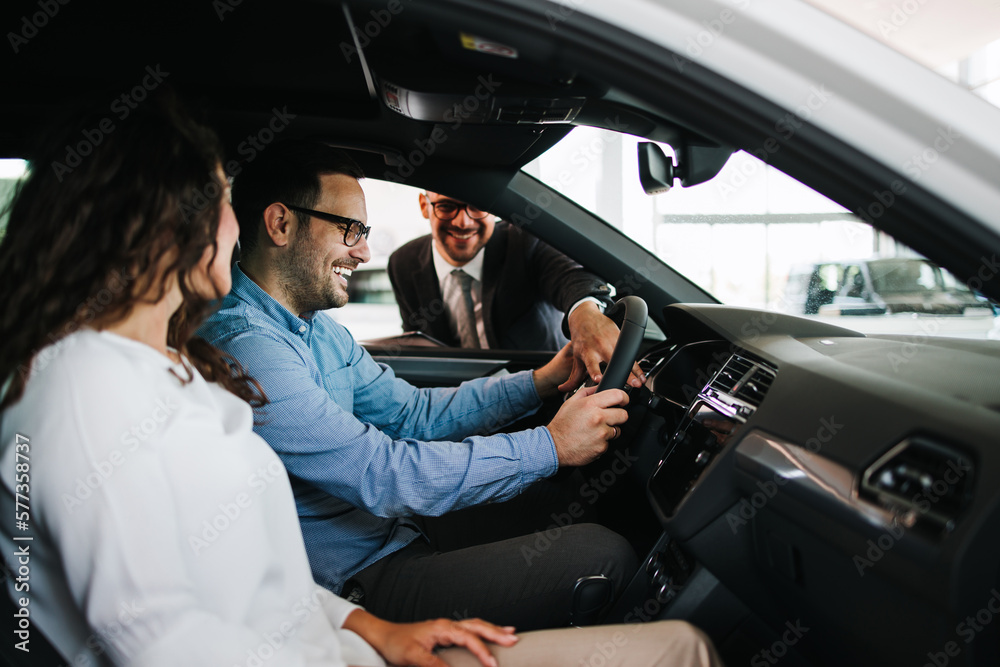 Middle age couple choosing and buying car at car showroom. Car salesman helps them to make right decision. Middle age couple choosing and buying car at car showroom. Car salesman helps them to make right decision.