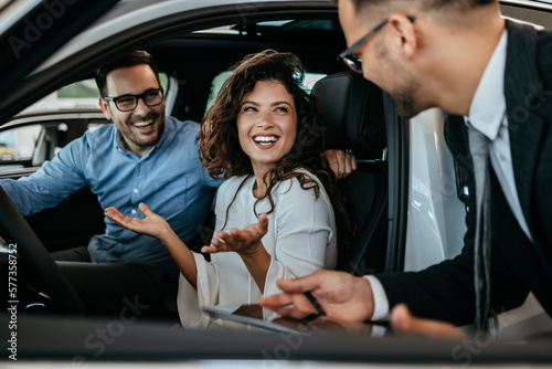 Middle age couple choosing and buying car at car showroom. Car salesman helps them to make right decision.