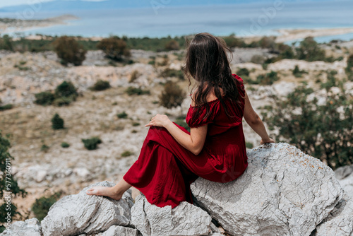 a girl on a rock by the sea in a red dress with dark hair