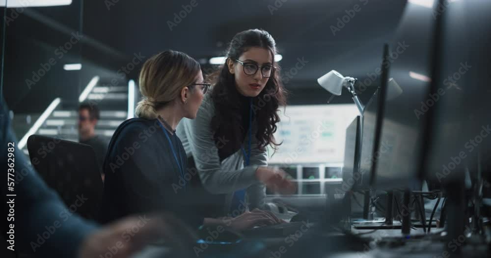 Two Diverse Colleagues Having a Conversation While Busy Working on a Team Project. Multiethnic Female Designer Talking with a Project Manager. Teamwork in Technology Laboratory Two Diverse Colleagues Having a Conversation While Busy Working on a Team Project. Multiethnic Female Designer Talking with a Project Manager. Teamwork in Technology Laboratory