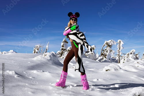 Winter fashion. Beautiful woman is wearing sexy winter clothing and winter hat and colorful boots and is posing in snow on mountains. Outdoor shoot.