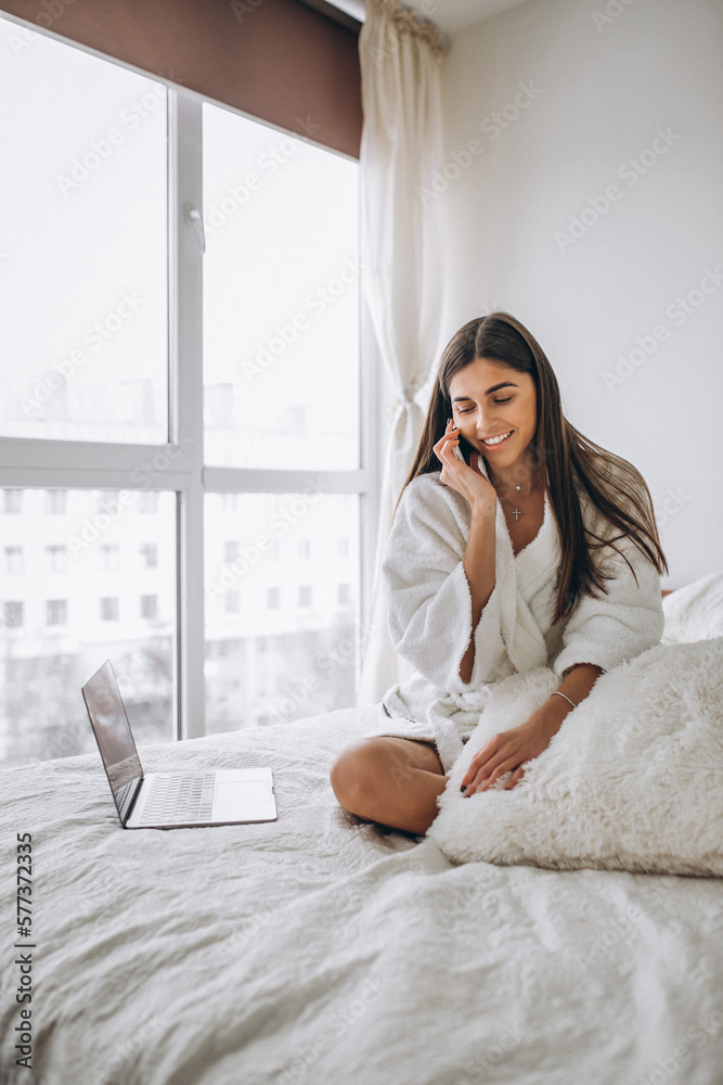 Woman working on computer in bed and talking on phone Woman working on computer in bed and talking on phone