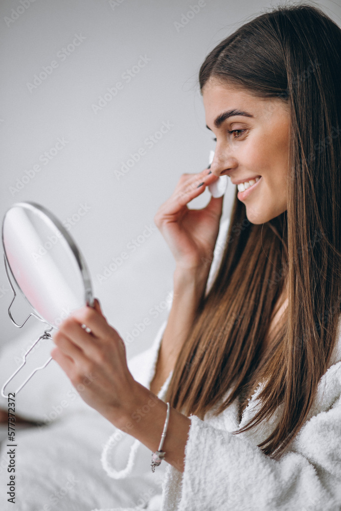Woman with mirror removing makeup with pad Woman with mirror removing makeup with pad