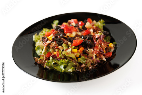 Delicious salad with lettuce, red pepper, tomato, corn and sliced olives on a black plate