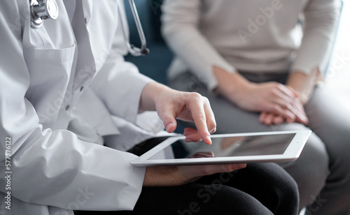 Doctor and patient sitting at sofa in clinic office. The focus is on female physician s hands using tablet computer  close up. Perfect medical service and medicine concept.