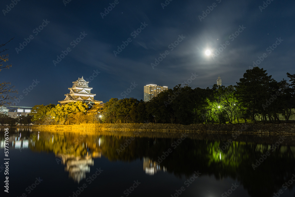日本　広島県広島市の広島市中央公園内にある夜になってライトアップされた広島城の天守閣と満月
