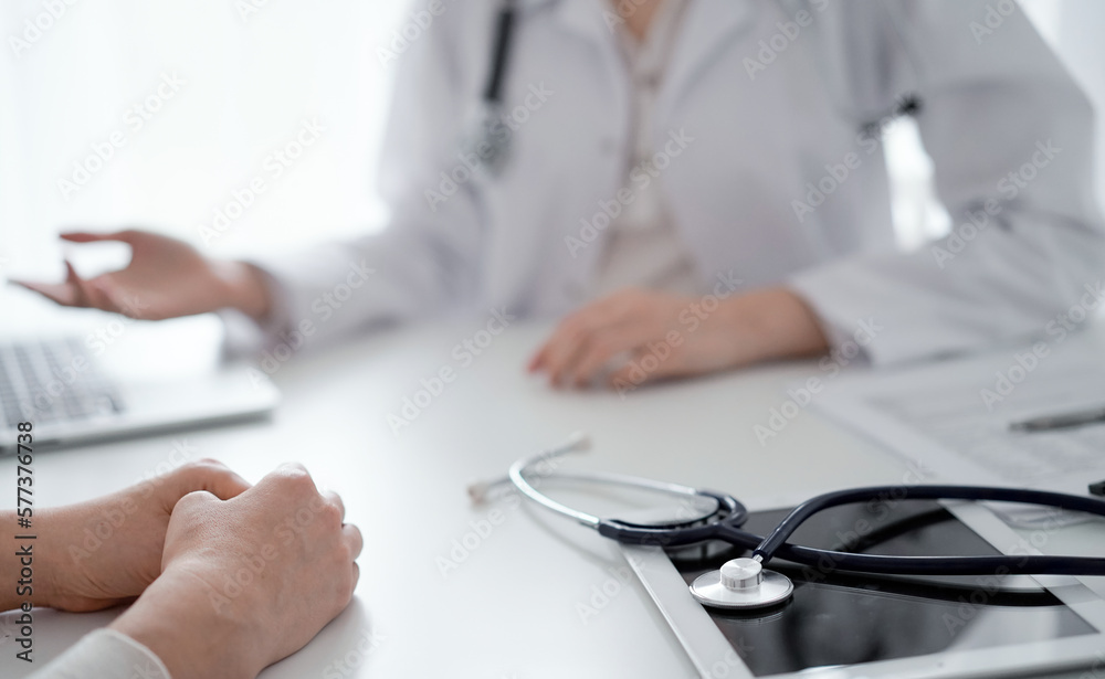 Doctor and patient sitting and discussing something at the desk in clinic. The focus is on the stethoscope lying on the table, close up. Medicine and healthcare concept Doctor and patient sitting and discussing something at the desk in clinic. The focus is on the stethoscope lying on the table, close up. Medicine and healthcare concept