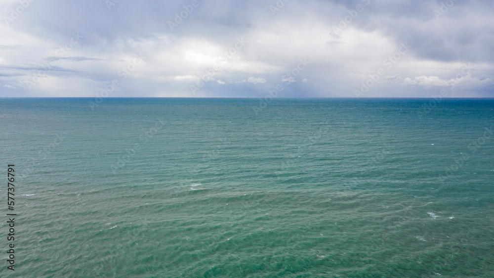 Aerial view of the sea with the horizon. The sky is cloudy and shades of blue color the sea water.