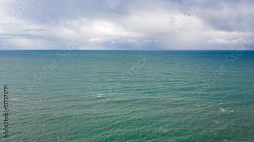 Aerial view of the sea with the horizon. The sky is cloudy and shades of blue color the sea water.