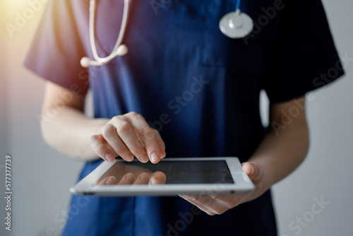 Doctor woman using tablet computer while standing near panorama window in clinic, close up. Physician or surgeon at work. Medicine concept. photo