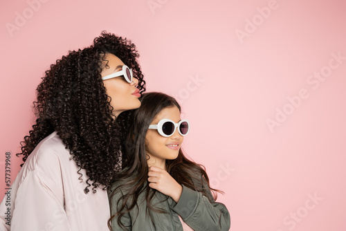 Trendy parent and child in sunglasses standing isolated on pink.