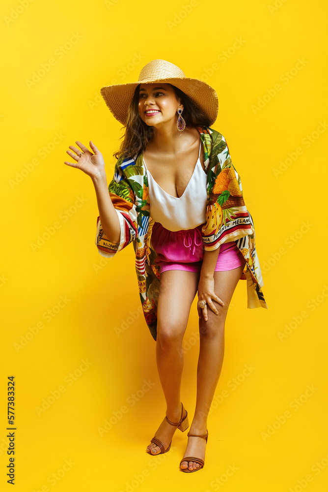 A girl with a Hispanic appearance in bright summer clothes and with a straw hat on a yellow background A girl with a Hispanic appearance in bright summer clothes and with a straw hat on a yellow background
