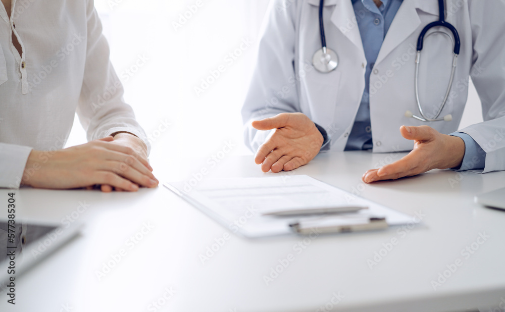 Doctor and patient discussing current health questions while sitting near of each other and using clipboard at the table in clinic, just hands closeup. Medicine concept. Doctor and patient discussing current health questions while sitting near of each other and using clipboard at the table in clinic, just hands closeup. Medicine concept.