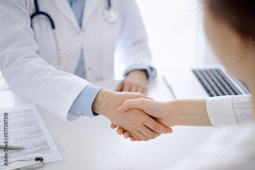 Doctor and patient shaking hands while sitting opposite of each other at the table in clinic, just hands close up. Medicine concept. © rogerphoto
