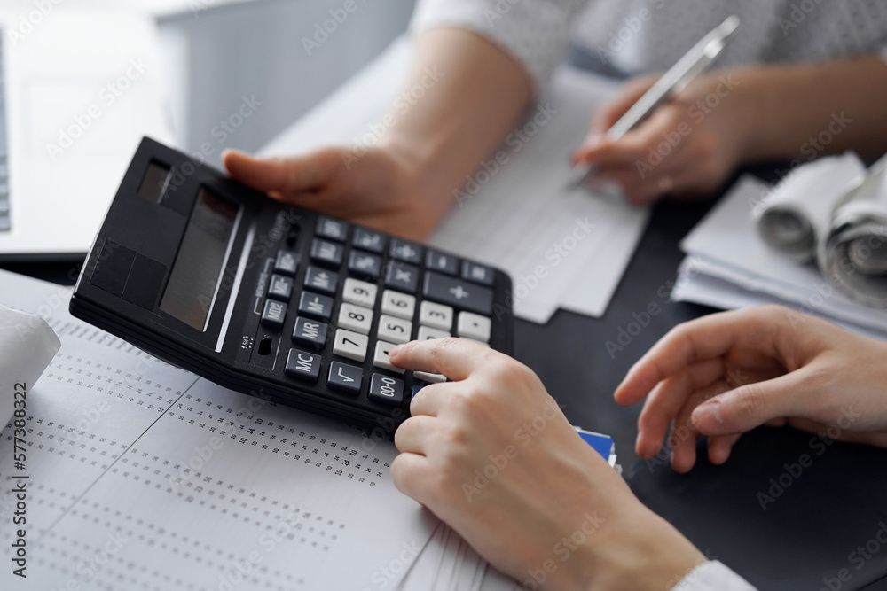 Woman accountant using a calculator and laptop computer while counting taxes for a client. Business audit and finance concepts. Woman accountant using a calculator and laptop computer while counting taxes for a client. Business audit and finance concepts.