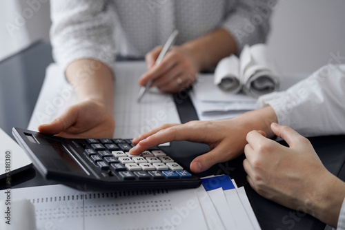 Woman accountant using a calculator and laptop computer while counting taxes for a client. Business audit and finance concepts. © rogerphoto