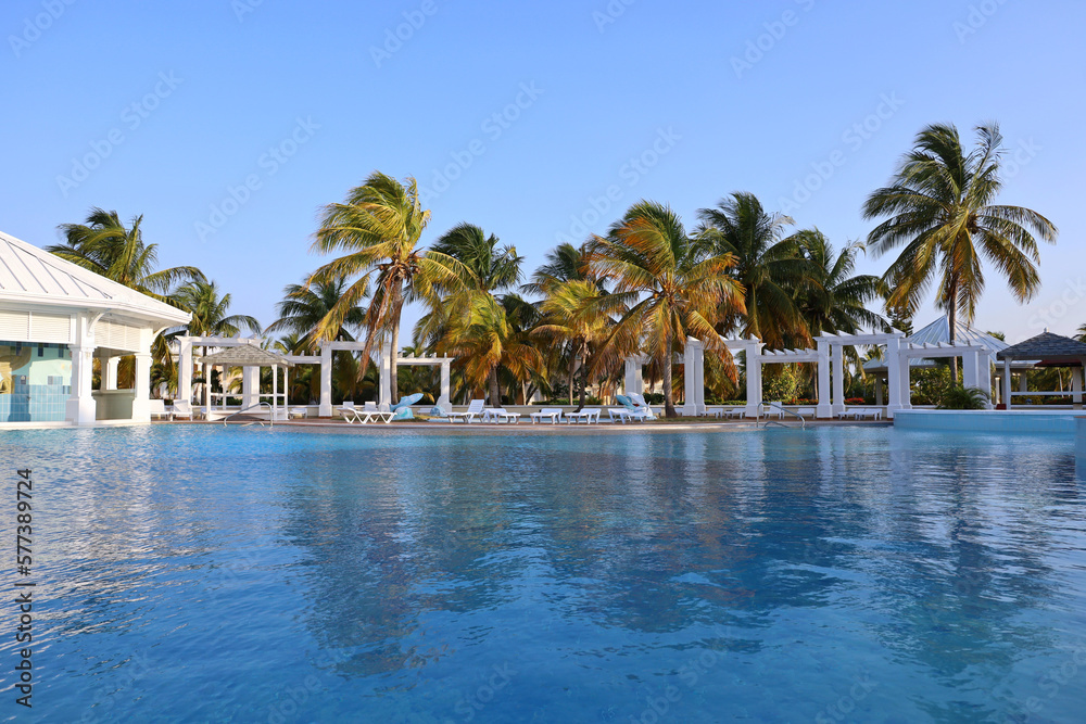 View to swimming pool and empty deck chairs against the palm trees. Vacation on beach resort on tropical island