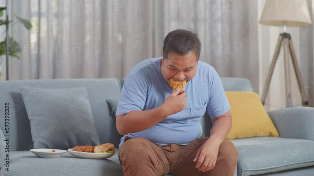 A Fat Asian Man Weighing Himself While Eating Fast Food Having Fried Chicken In The Living Room At Home
A Fat Asian Man Weighing Himself While Eating Fast Food Having Fried Chicken In The Living Room At Home