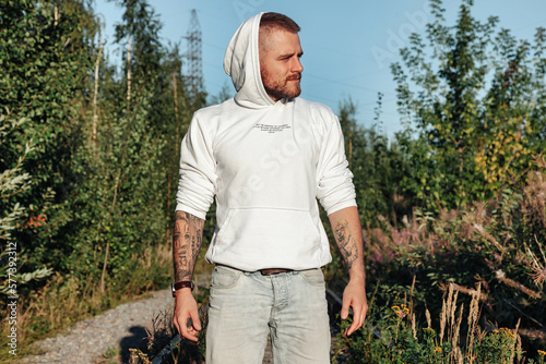 Bearded jewish guy in white jacket standing at forest, looking away. Man spending summertime in countryside outdoor. Lifestyle concept walking in fresh air on nature. Copy advertising text space