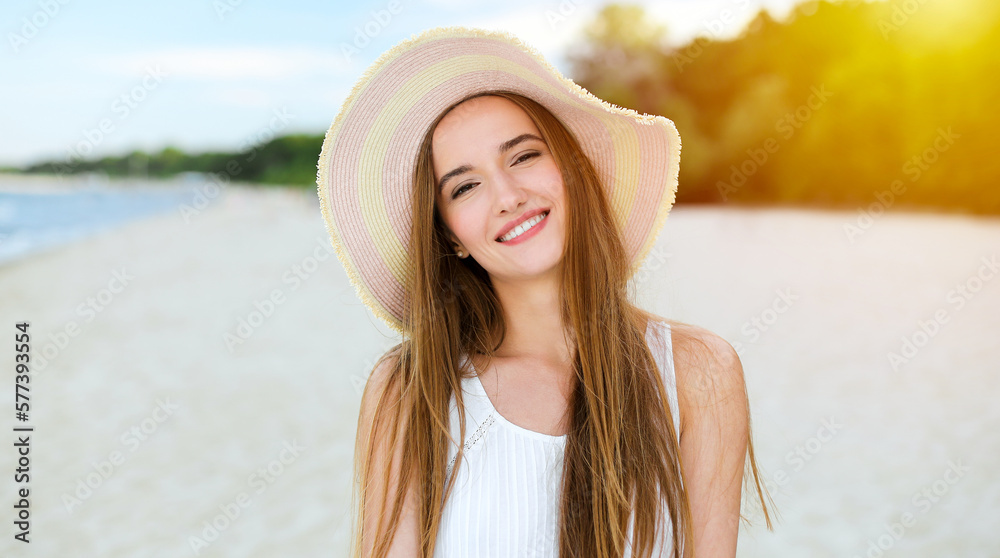 Portrait of a happy smiling woman in free happiness bliss on ocean beach standing with a hat. A female model in a white summer dress enjoying nature during travel holidays vacation outdoors.