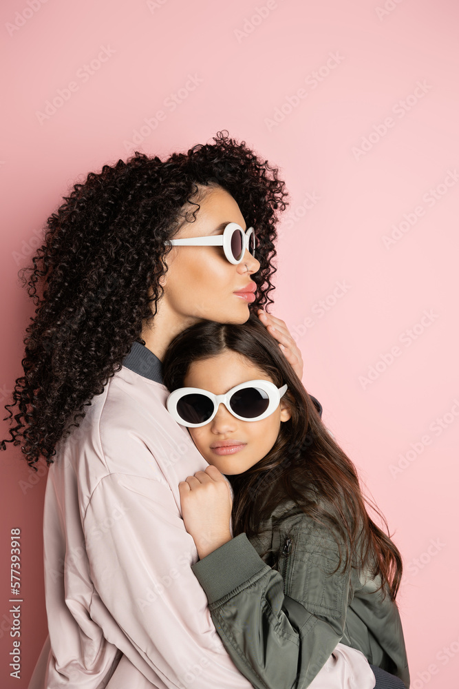 Trendy woman in sunglasses hugging preteen kid on pink background. Trendy woman in sunglasses hugging preteen kid on pink background.