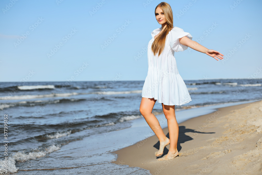 Happy smiling beautiful woman is walking on the ocean beach with open arms. Happy smiling beautiful woman is walking on the ocean beach with open arms.