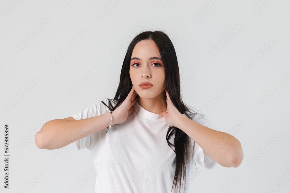 Portrait of a Beautiful brunette Girl with straight long hair, holding hands on her neck dressed in a white shirt. Isolated on white. Portrait of a Beautiful brunette Girl with straight long hair, holding hands on her neck dressed in a white shirt. Isolated on white.