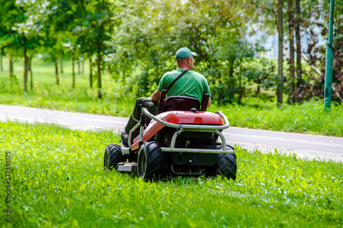 Fototapeta Naklejka Na Ścianę i Meble -  A man on a lawn mower in a summer park