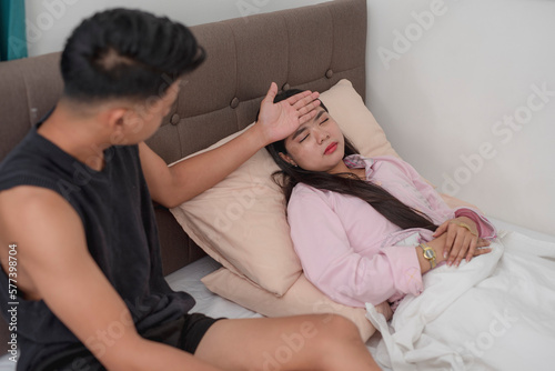 A young man checks his girlfriend's temperature with his hand. A loving partner taking care of his sick wife resting in the bed.