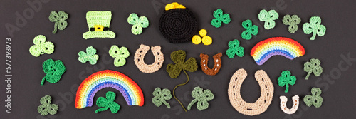 St Patrick's Day concept. Knitted composition of a green hat, a pot of gold, a horseshoe, a rainbow and green shamrocks on a black background. Banner