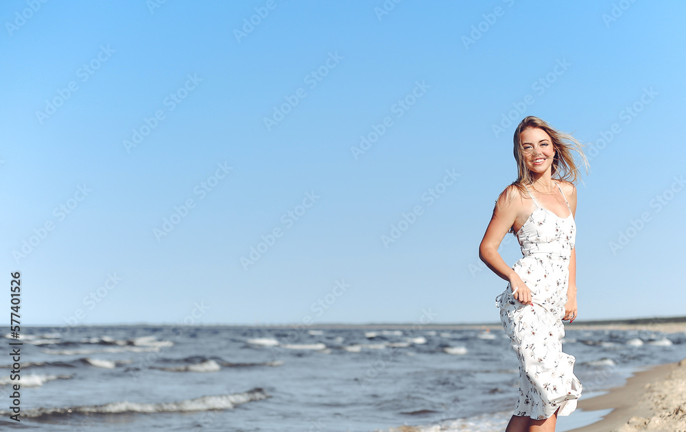 Happy blonde woman in free happiness bliss on ocean beach standing straight. Portrait of a female model in white summer dress enjoying nature during travel holidays vacation outdoors Happy blonde woman in free happiness bliss on ocean beach standing straight. Portrait of a female model in white summer dress enjoying nature during travel holidays vacation outdoors