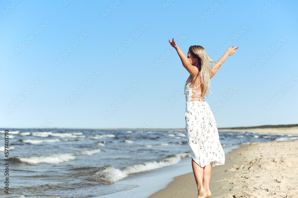 Happy blonde beautiful woman on the ocean beach standing in a white summer dress, open arms. Happy blonde beautiful woman on the ocean beach standing in a white summer dress, open arms.