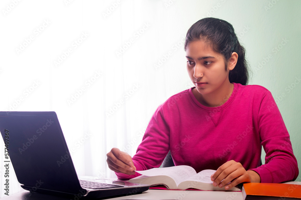 Young girl reading book front of Laptop Young girl reading book front of Laptop