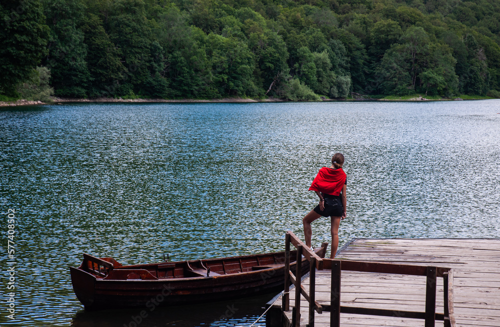 A young girl standing on the wooden dock next to a wooden boat. Biogradsko lake in Montenegro.
