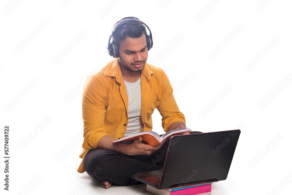 Teenager wearing headphones holding book and using laptop Teenager wearing headphones holding book and using laptop