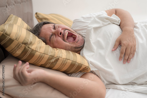A man screams due to excruciating pain while lying on the bed. An severe bout of heartburn or GERD. photo
