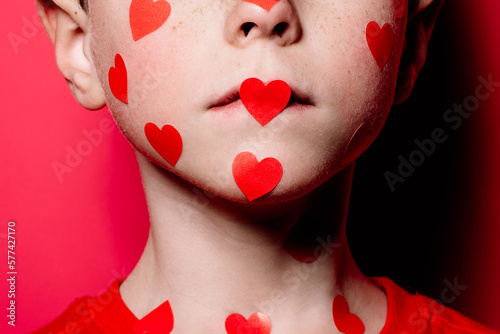 Anonymous cute boy in red casual shirt with red love sticker on face while posing for photograph photo