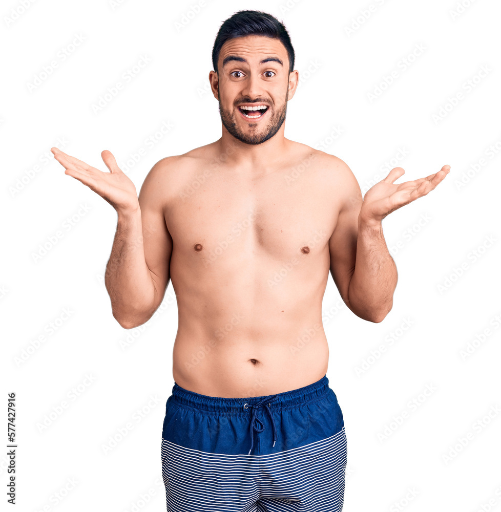Young handsome man wearing swimwear celebrating victory with happy smile and winner expression with raised hands Young handsome man wearing swimwear celebrating victory with happy smile and winner expression with raised hands