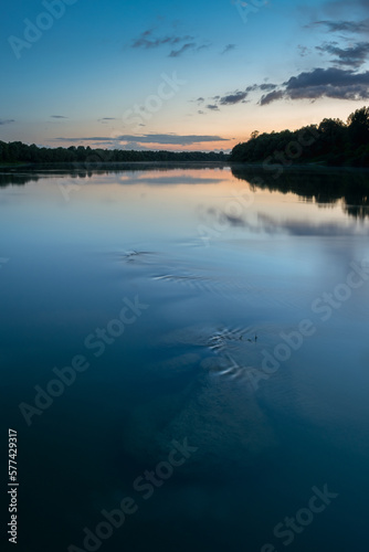 Underwater boulders in river at dusk  landscape of Sava river with forest silhouette on shore and clouds reflecting in water