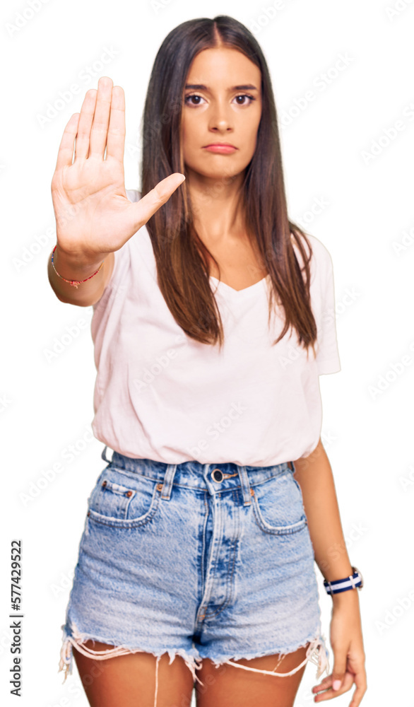 Young hispanic woman wearing casual white tshirt doing stop sing with palm of the hand. warning expression with negative and serious gesture on the face. Young hispanic woman wearing casual white tshirt doing stop sing with palm of the hand. warning expression with negative and serious gesture on the face.