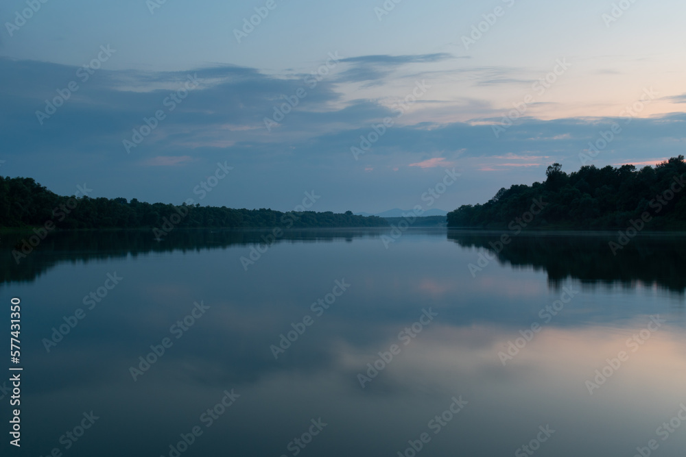 Landscape of cloudy twilight with symmetric reflection on water surface, distant mountain in haze