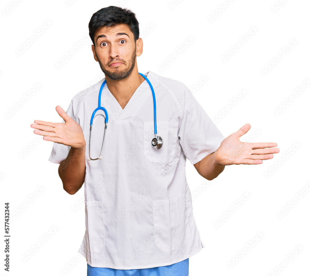 Young handsome man wearing doctor uniform and stethoscope clueless and confused expression with arms and hands raised. doubt concept. Young handsome man wearing doctor uniform and stethoscope clueless and confused expression with arms and hands raised. doubt concept.