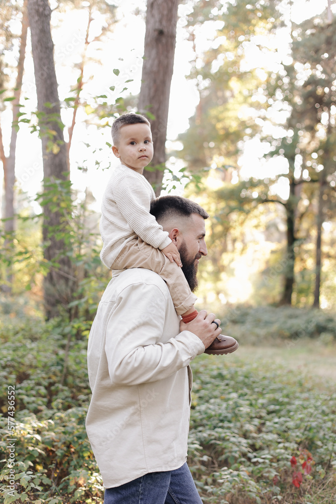 Father's day. Smiling dad holding his toddler son on shoulders look at camera outdoor at nature. Family spend and enjoy time together. Happy fatherhood and childhood, family love, togetherness concept Father's day. Smiling dad holding his toddler son on shoulders look at camera outdoor at nature. Family spend and enjoy time together. Happy fatherhood and childhood, family love, togetherness concept